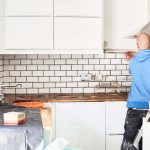 How kitchen tiles are different from bathroom tiles A man working in a new kitchen, a tiler applying tiles to the wall behind the cooker.
